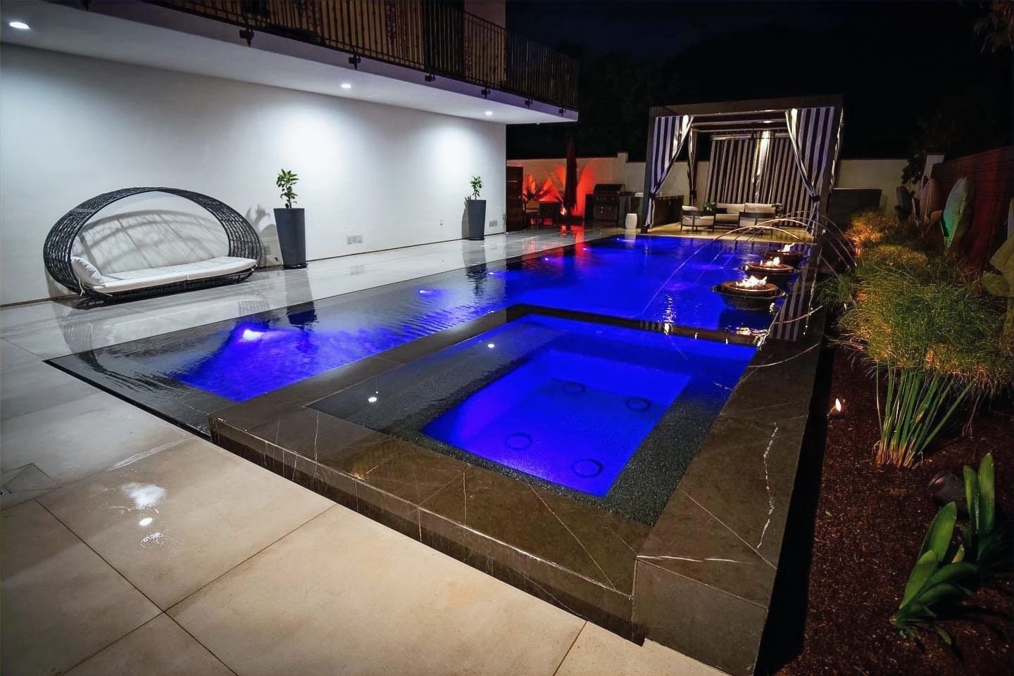 Pool and spa with blue lighting, fire bowls and a covered lounge