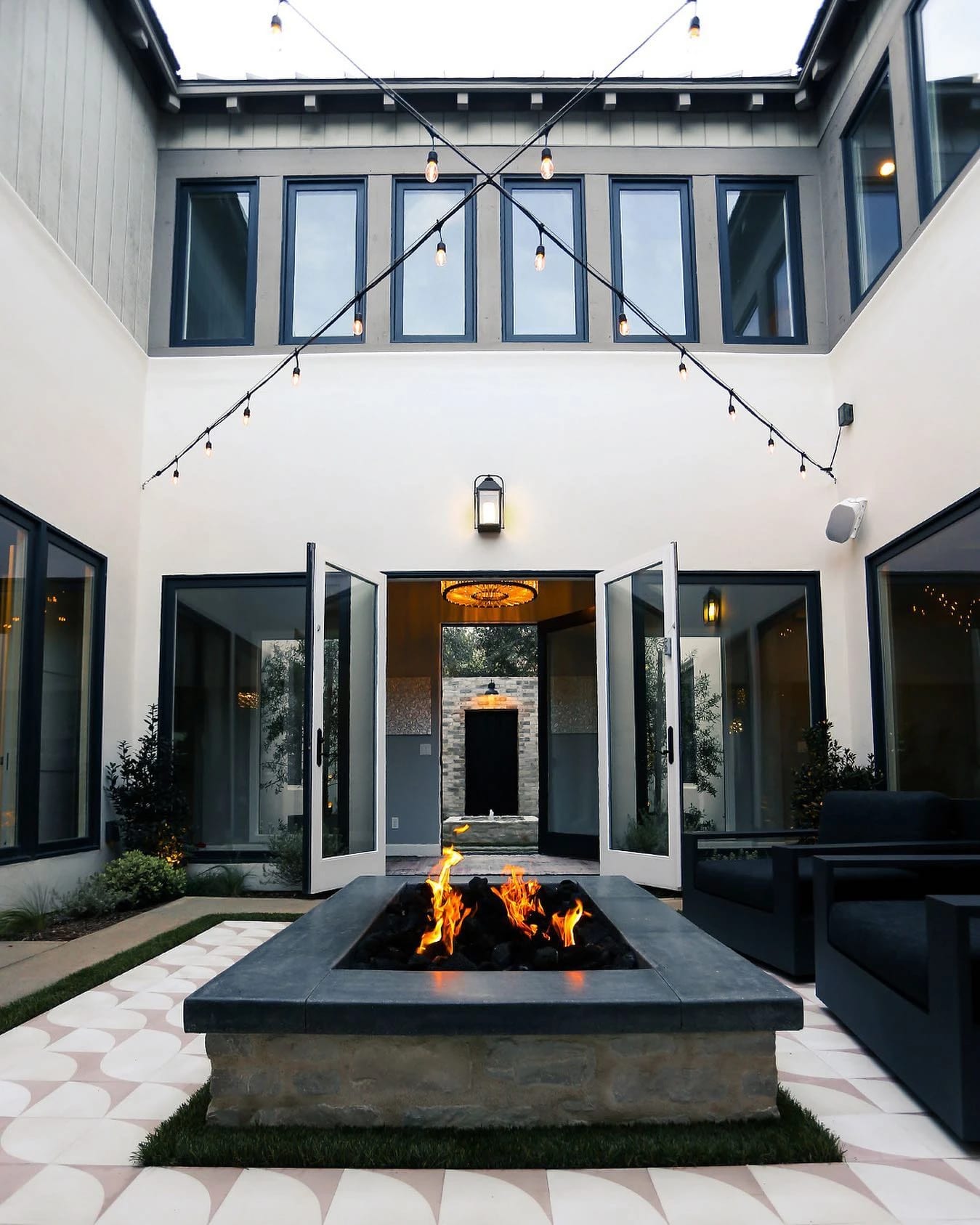 Courtyard with a central stone fire feature, glass doors and string lights