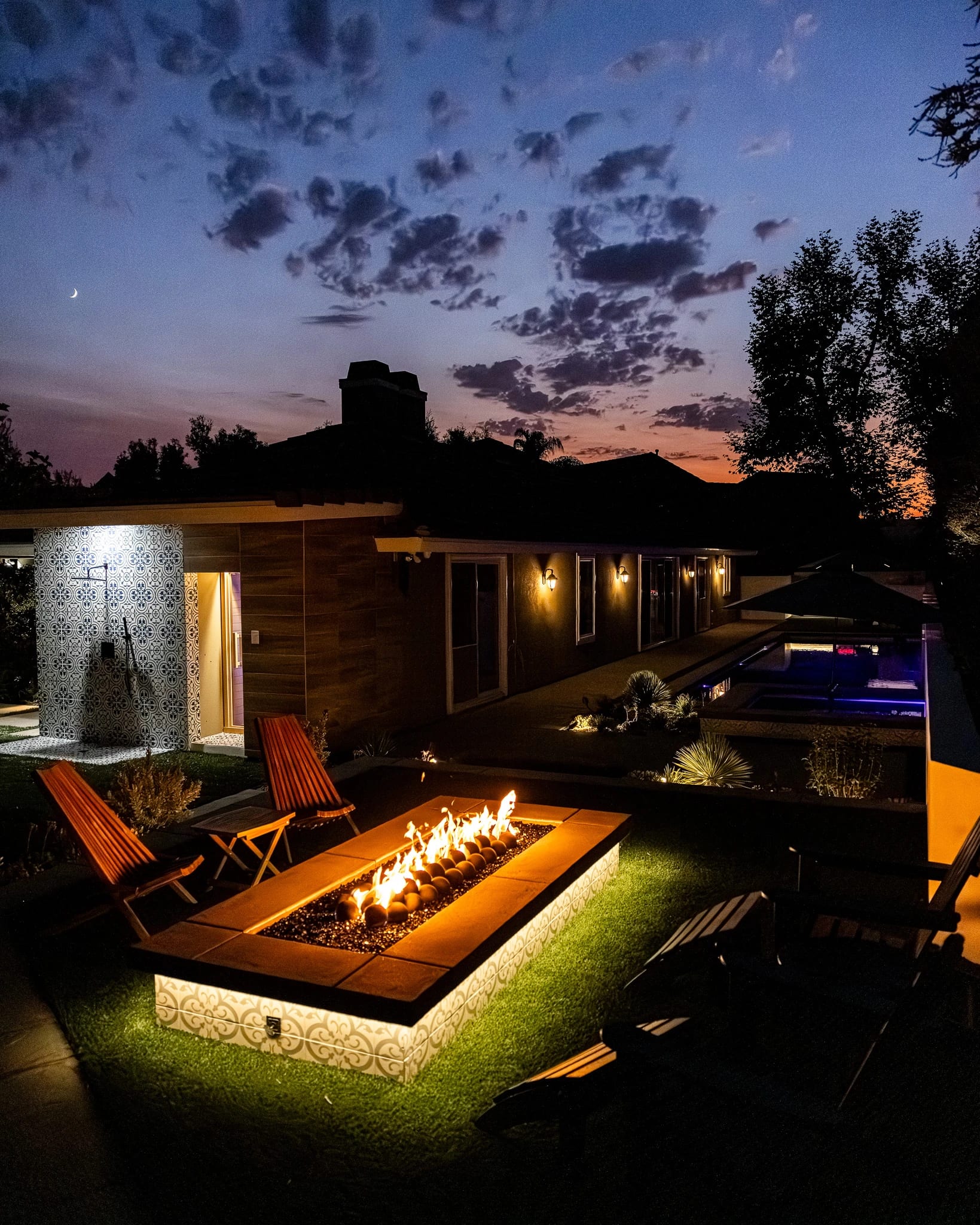 Backyard fire pit terrace lit at night with a lap pool below