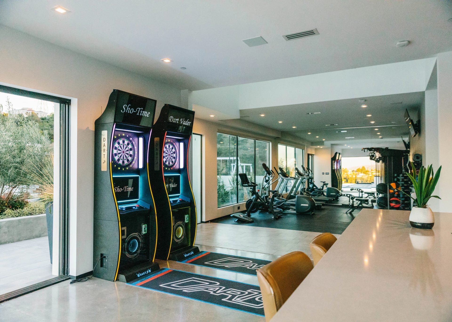 Entertainment room with arcade dartboards opening onto a home gym