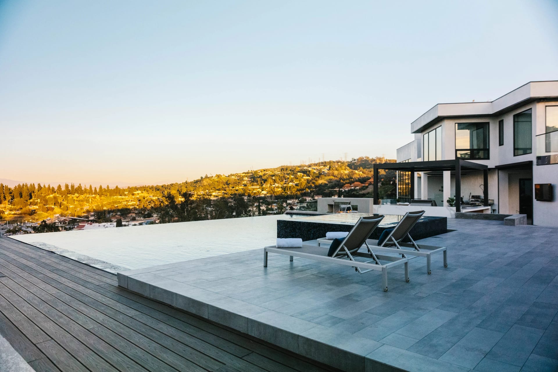 An infinity pool and sun loungers overlooking the California hills beside a modern residence
