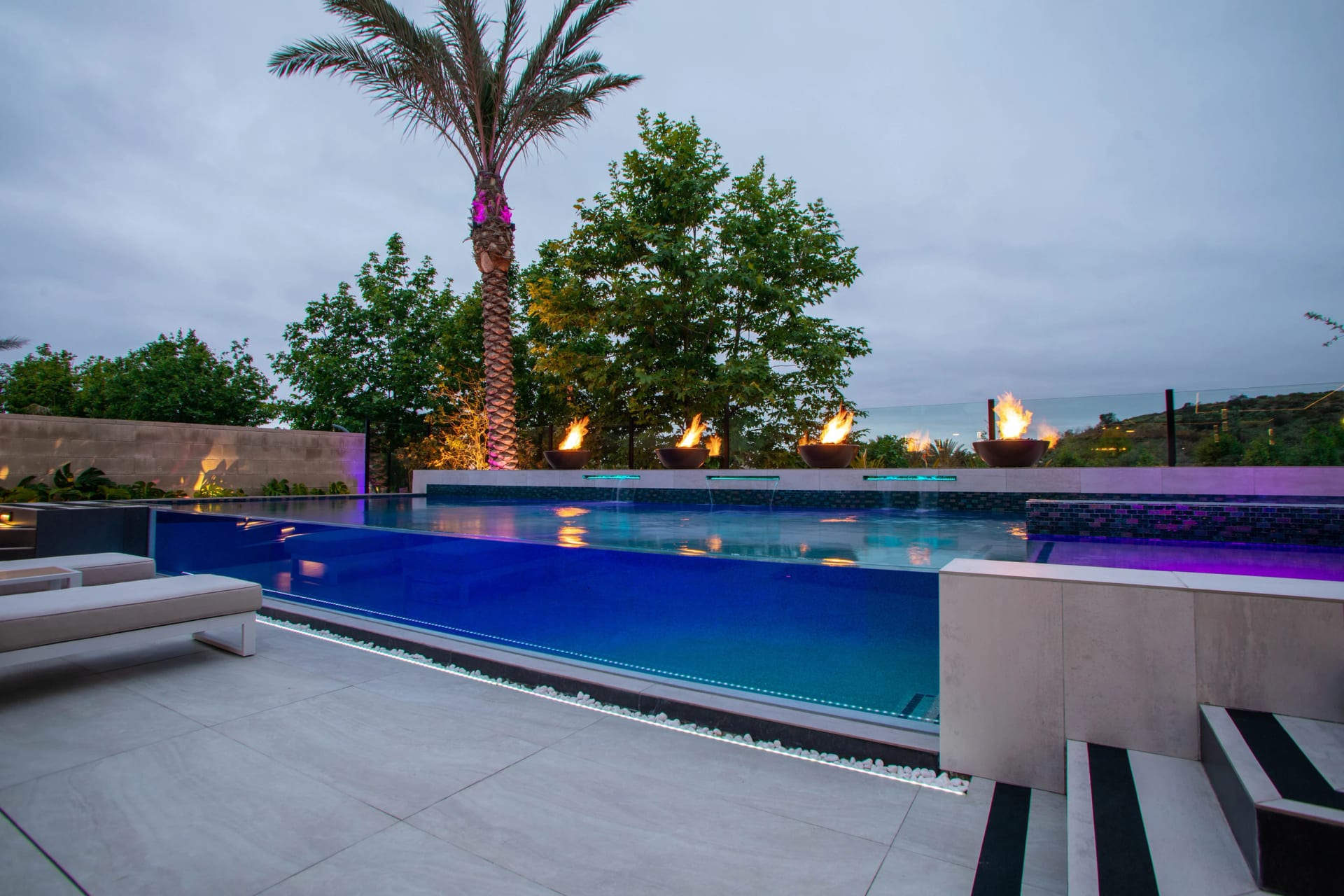 Infinity pool with colored underwater lighting at dusk beside a palm