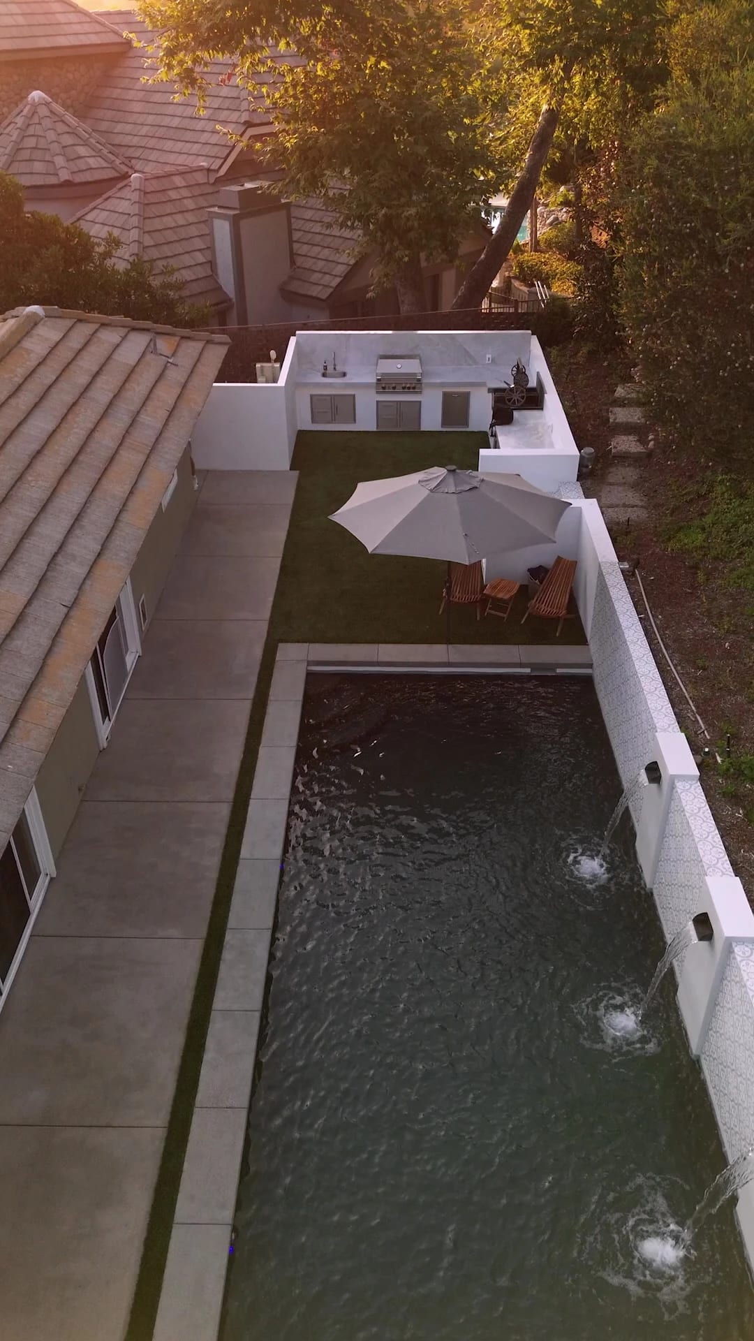 Aerial view of a narrow lap pool with a fountain wall beside a house