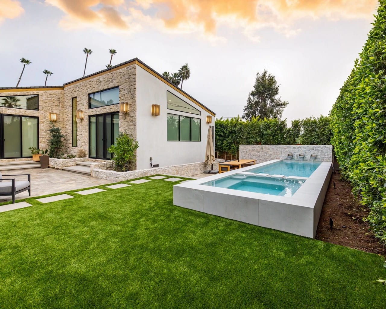 Backyard lawn with a raised spa beside a stone and stucco home at sunset