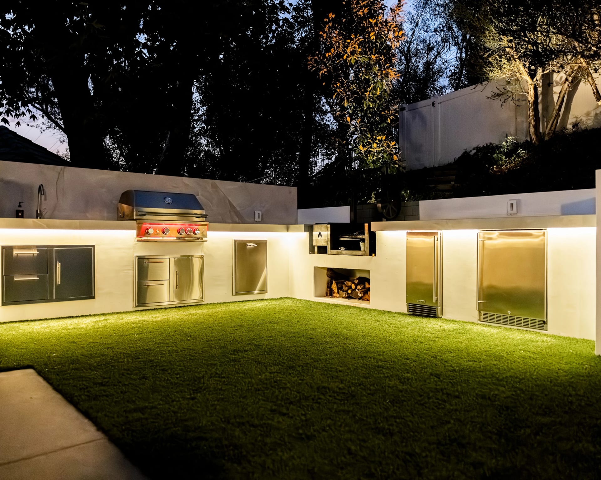 Outdoor kitchen and lounge wall lit at night beside a lawn