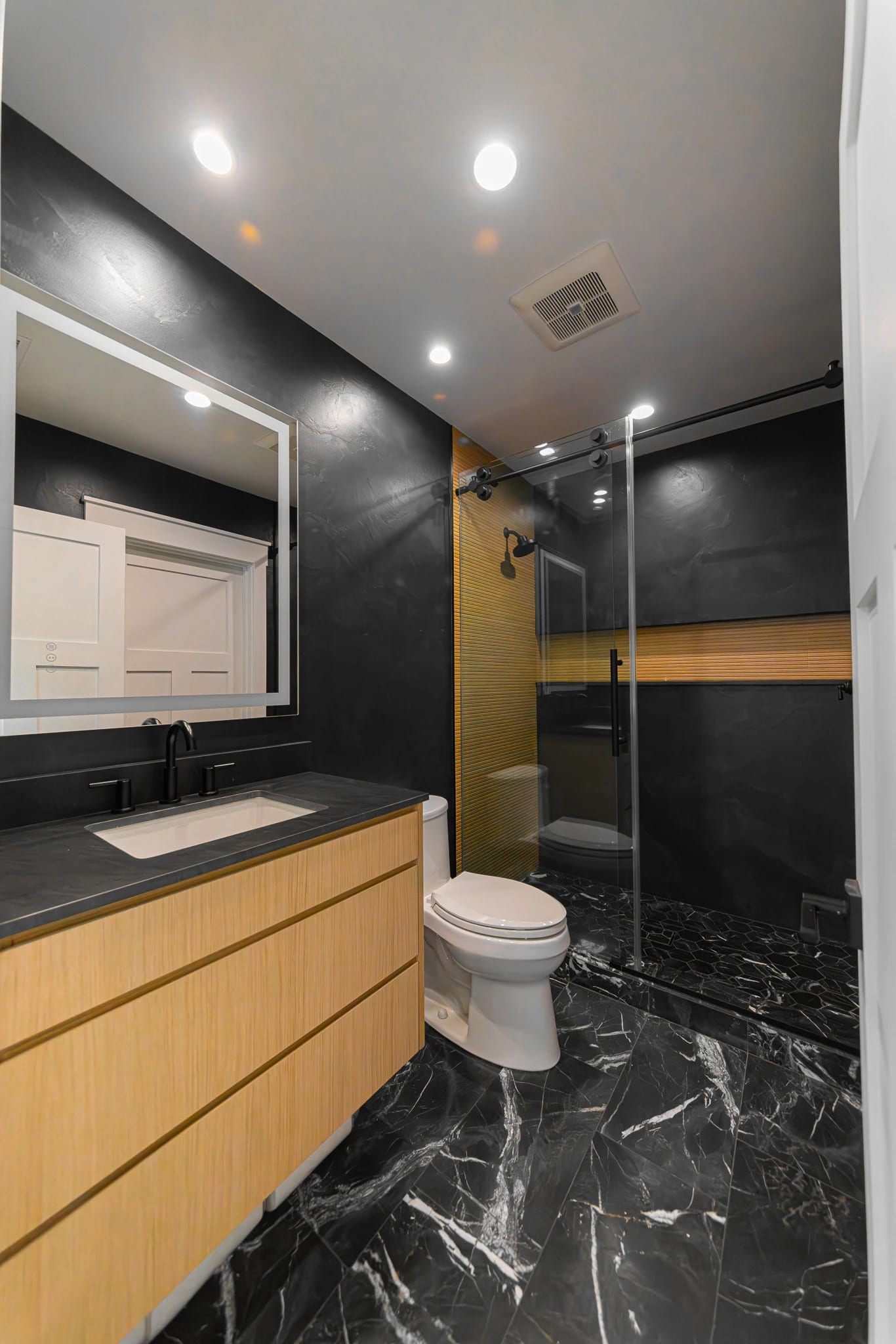 Bathroom with black marble walls and warm wood cabinetry