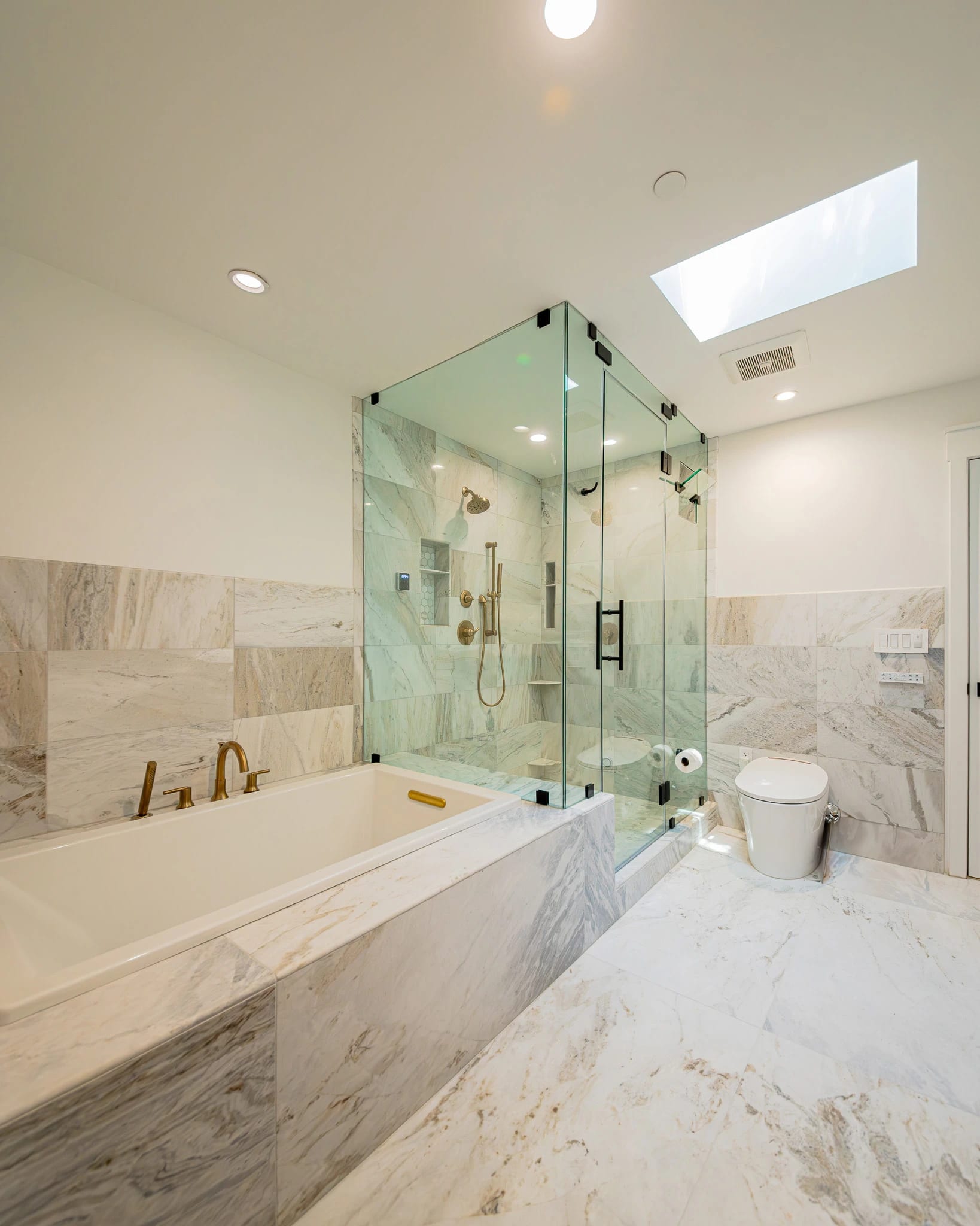 Bathroom with a marble tub surround and a glass shower under a skylight