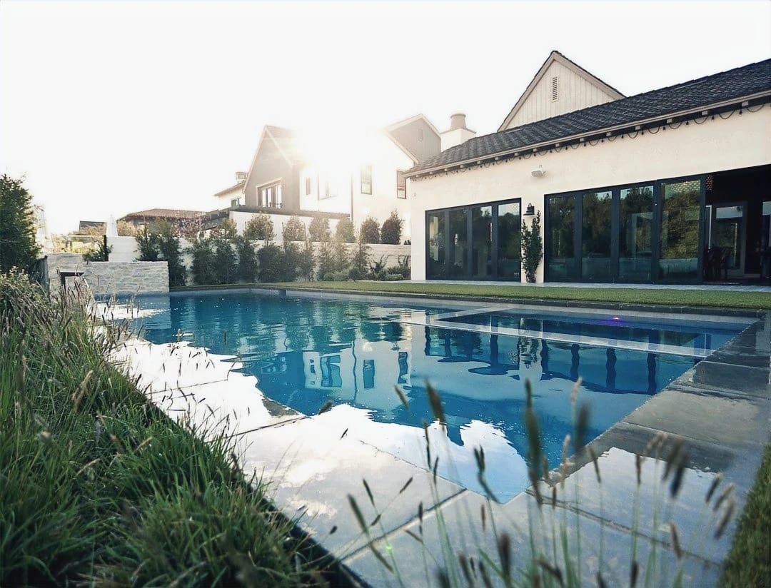 Backyard pool reflecting the house, with greenery and stone around it