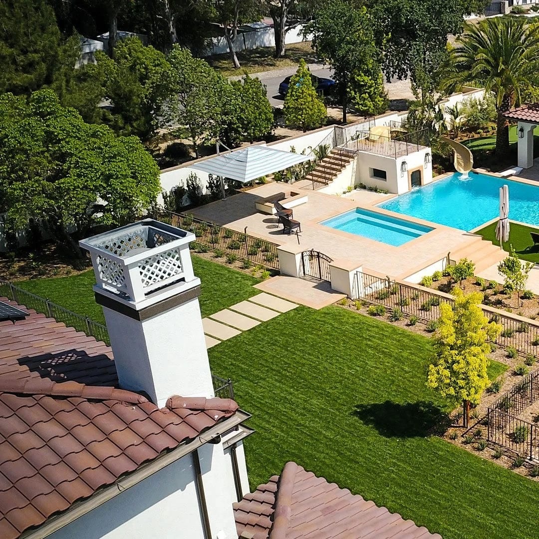 Aerial view of a pool and lawn behind a Spanish-style home