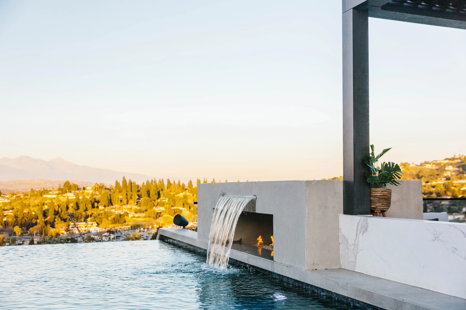 Pool with a sheer waterfall feature and hillside views at sunset