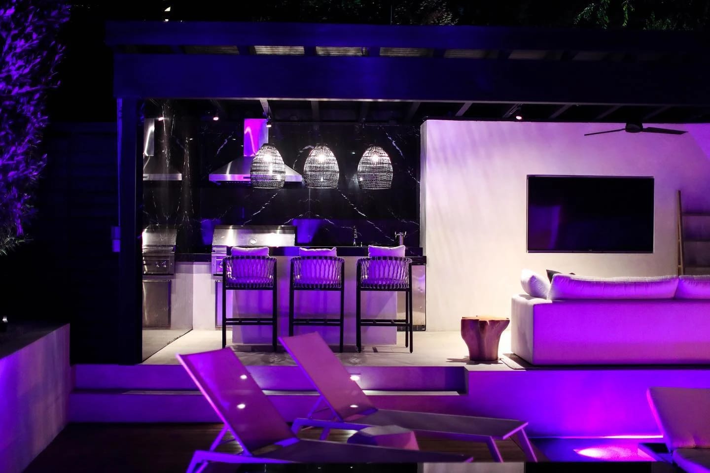 Outdoor bar with a black marble backsplash, stools and purple accent lighting