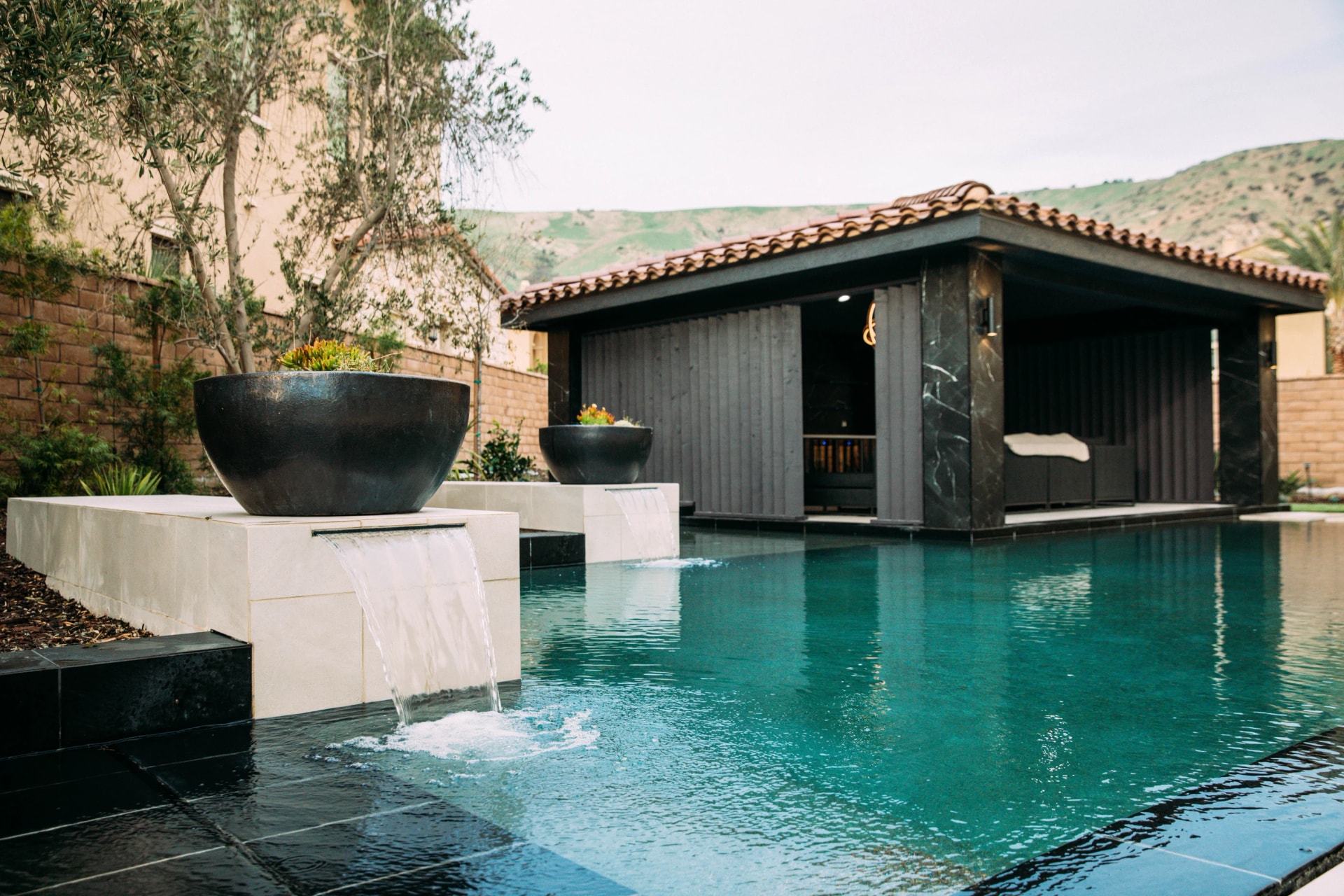 Turquoise courtyard pool with stone water features and a dark timber poolside pavilion