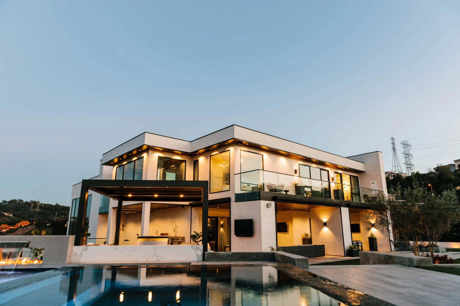 A contemporary California residence with illuminated interiors, glass balconies, and a reflective pool at dusk