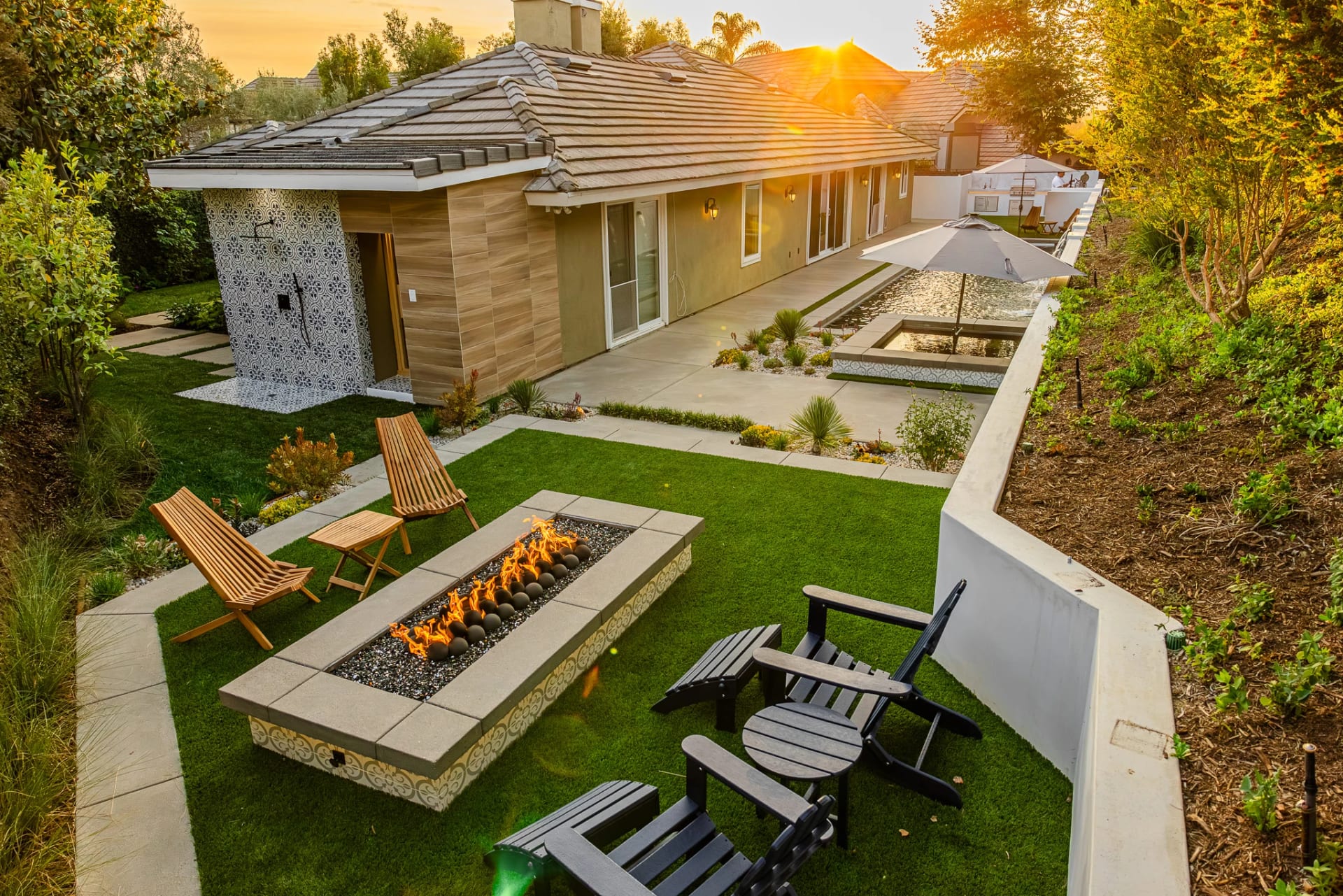 A garden pavilion with an outdoor fireplace, green lawn, and integrated seating